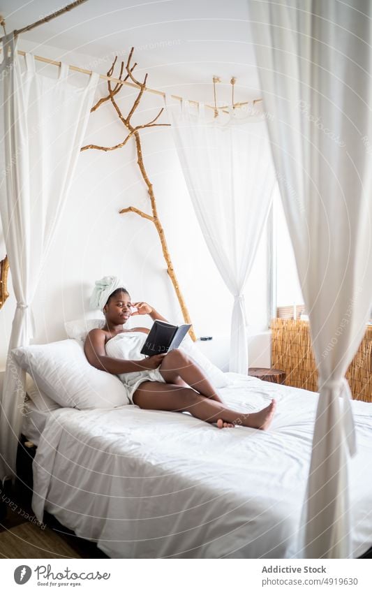 Black woman lying on a bed while reading a book black notebook care beauty relaxation female therapy young spa beautiful wellness healthy luxury body paper