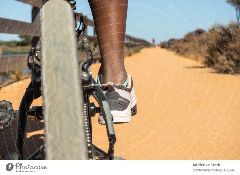 Anonymous black woman riding a bike wheel bicycle leg isolated transportation path biking object sand activity symbol ride race speed summer sunny fitness