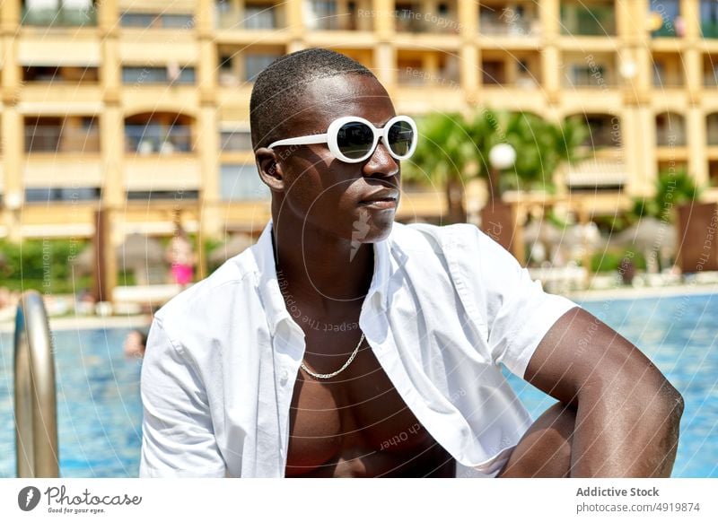 Black man sitting on poolside rest recreation swimming chill pastime tropical resort sunglasses black african american travel fit masculine free time enjoy male