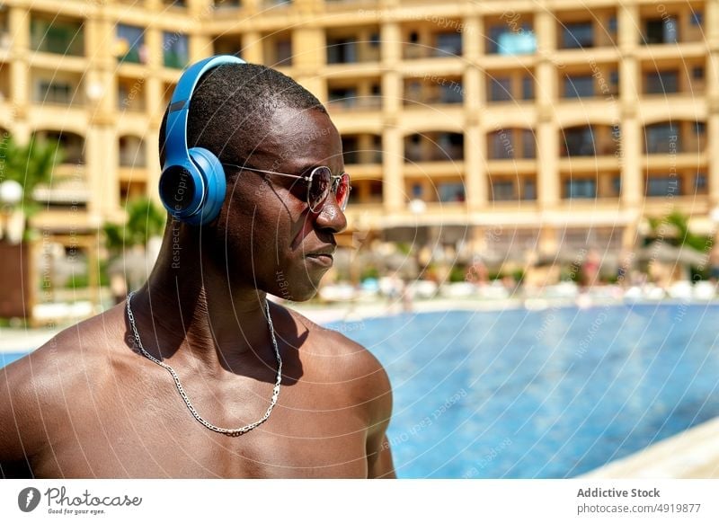 Black man listening to music near swimming pool rest recreation song hobby pastime sound headphones male masculine audio confident playlist free time melody