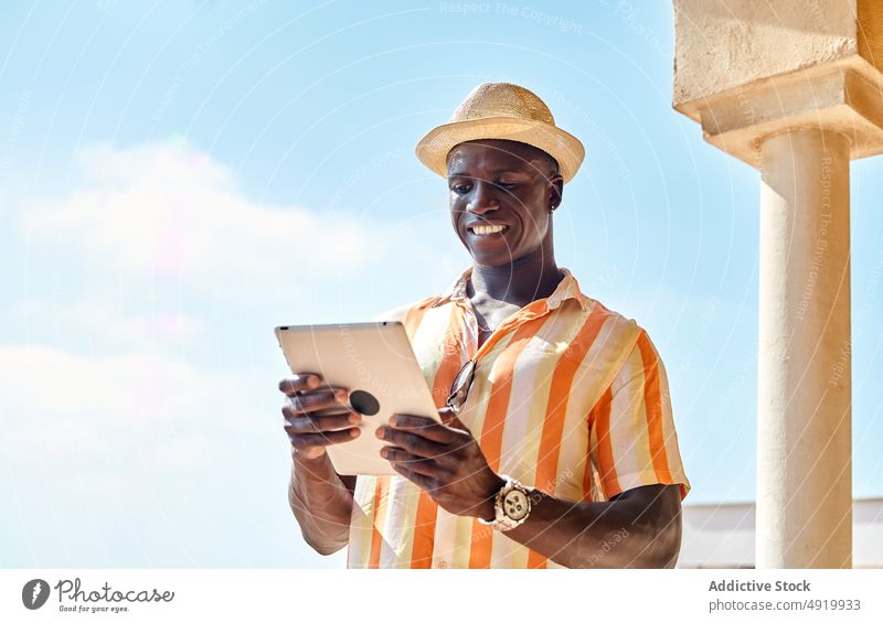 Black man browsing tablet on sunny summer day businessman resort sea tropical online internet coast street black shore african american surfing ethnic pillar