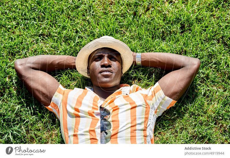Black man lying on lawn rest relax summer field dreamy pastime park chill leisure confident african american black grass hat male ethnic casual grassy calm