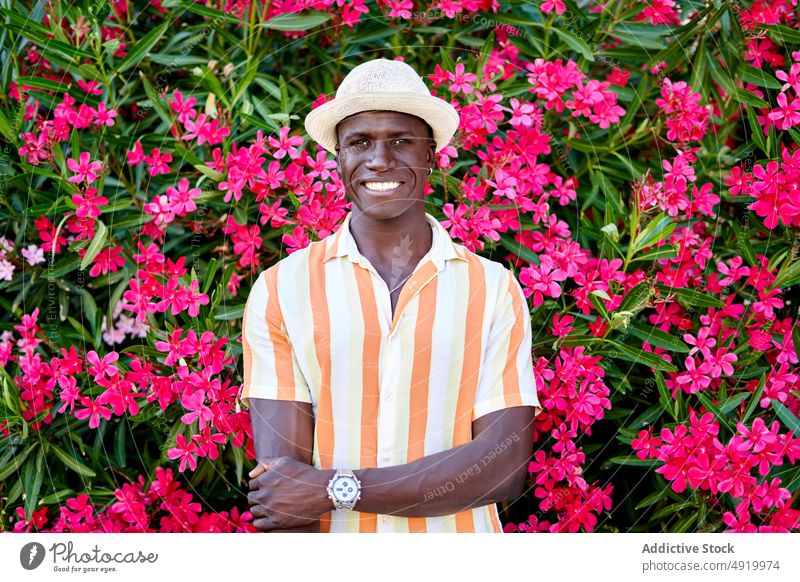 Happy black man near blooming bush street flower plant appearance city floral attire style african american ethnic summer male guy town entrepreneur modern hat