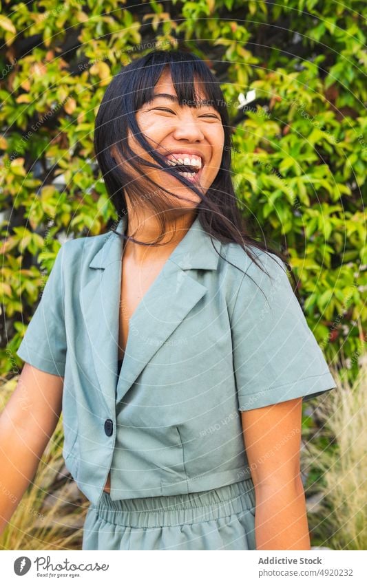 Happy Asian woman in park laugh bush lush happy weekend style summer daytime female ethnic asian young cheerful carefree eyes closed optimist joke excited glad