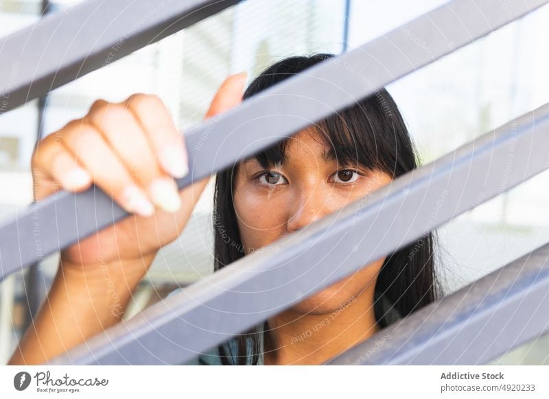 Asian woman behind gray fence rest street touch calm building urban dark hair brown eyes female young asian ethnic modern individuality appearance black hair