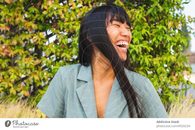 Happy Asian woman in park laugh bush lush happy weekend style summer daytime female ethnic asian young cheerful carefree eyes closed optimist joke excited glad