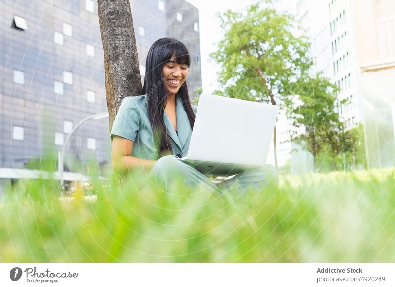 Female student using laptop near tree woman cheerful homework lawn education glad park study female happy young summer device smile gadget knowledge online