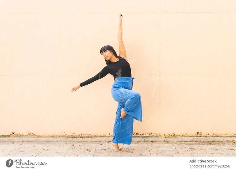 Barefoot ethnic dancer stretching on street woman flexible bend wall pavement leg raised female young asian balance building perform choreography daytime