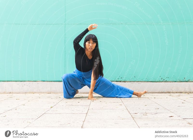 Asian woman dancing on pavement dance street grace wall arm raised touch lunge urban female young asian ethnic energy talent barefoot long hair black hair