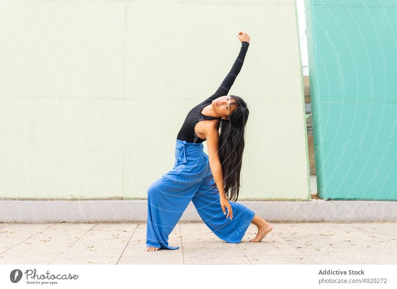 Asian woman dancing on pavement dance street grace wall arm raised lunge urban female young asian ethnic energy talent barefoot long hair black hair practice