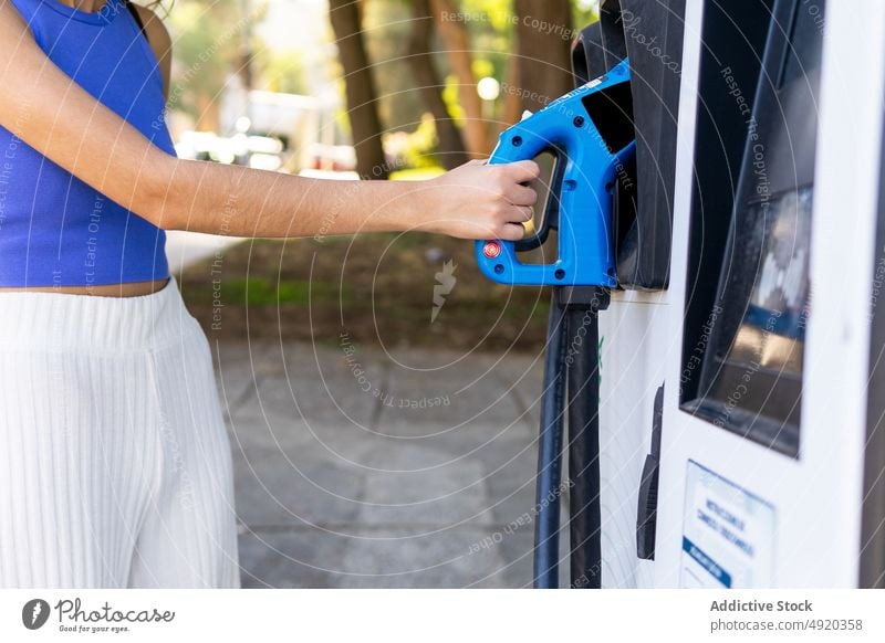 Anonymous woman taking pump nozzle at gas station petrol city electric gasoline car refuel positive modern driver convenient urban pistol power dispenser summer