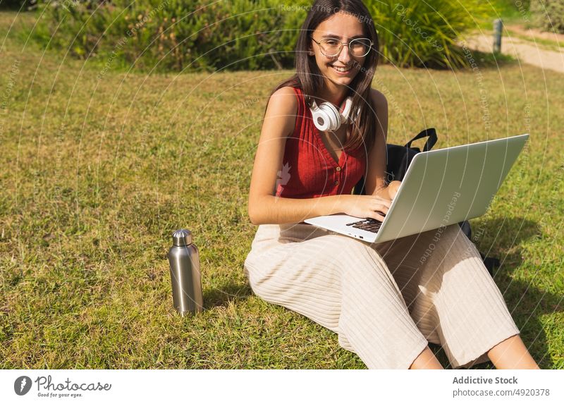 Woman studying on laptop in park woman student lawn homework looking at camera education knowledge learn online browsing typing city netbook academic street