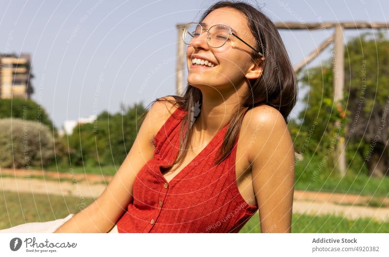 Happy woman resting on lawn park enjoy carefree pastime chill feminine summer smile positive city female cheerful tree eyeglasses young casual content eyewear