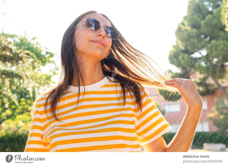 Young female touching hair in park woman smile touch hair summer rest weekend daytime sunny happy dark hair young style optimist sunglasses glad positive chill