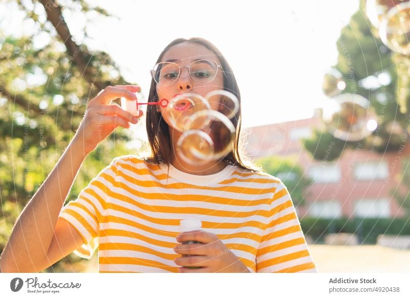 Young woman blowing soap bubbles park summer weekend daytime free time brunette rest female young relax lifestyle glasses season chill sunlight holiday casual