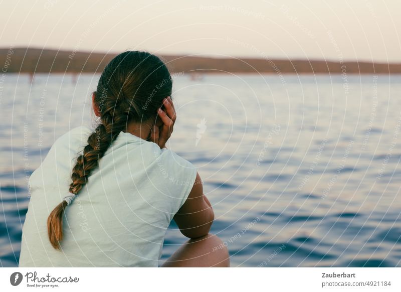 Girl with braid sits by the sea lost in thought Braids thoughts Ocean Evening outlook Meditative Future Fate brood Think ponder Waves Water Emotions hair