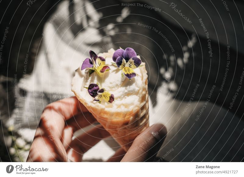 Hand holding an ice cream decorated with pansies, contrast light, aesthetic summer mood styled aesthetic food candid hard light sun direct sun vacation treat
