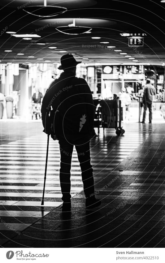 Man walks through train station on a stick black-white Descent step Dark Stagger Legs Old town Metal Metal grid Metal railings Diagonal light and dark Bright