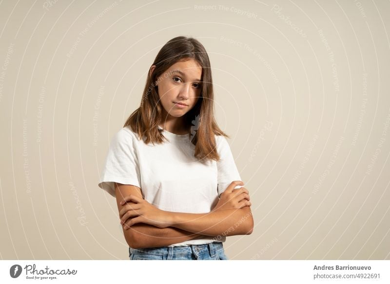 Portrait of angry hispanic teenage girl with arms crossed in warning gesture, isolated on beige studio background. upset casual female young brunette frustrated
