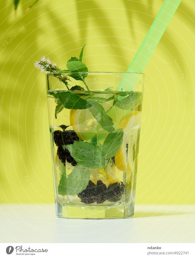 Transparent glass with lemonade, mint leaves, lemon slices and blackberries in the middle. Green background drink fruit fresh cold beverage cocktail summer