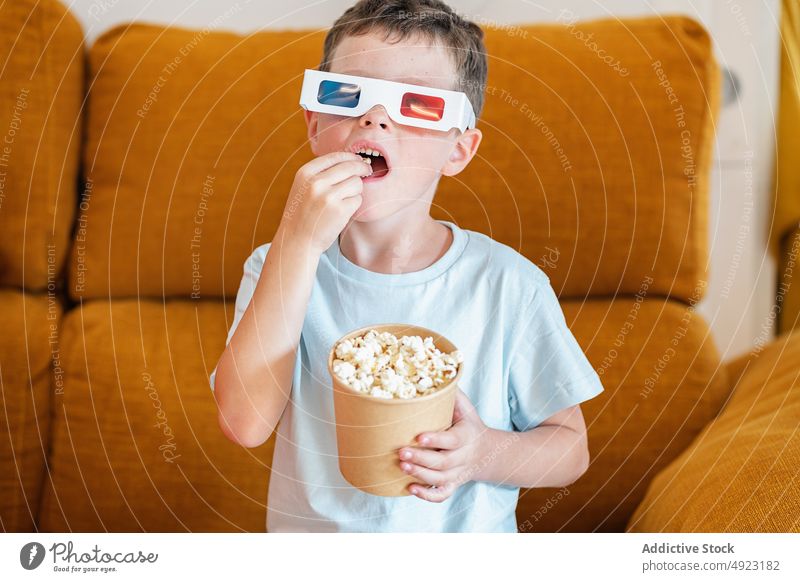 Boy in 3D glasses eating popcorn while watching movie kid boy 3d show snack showtime home food content glad optimist demonstrate reach out calorie television
