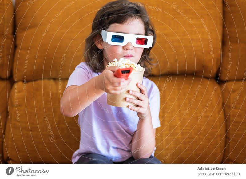 Girl in 3D glasses with popcorn watching movie kid girl remote control change 3d showtime channel snack controller food calorie television entertain realistic