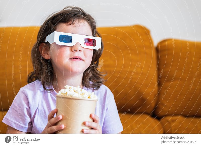 Girl in 3D glasses with popcorn watching movie kid girl remote control change 3d showtime channel snack controller bucket food calorie television entertain