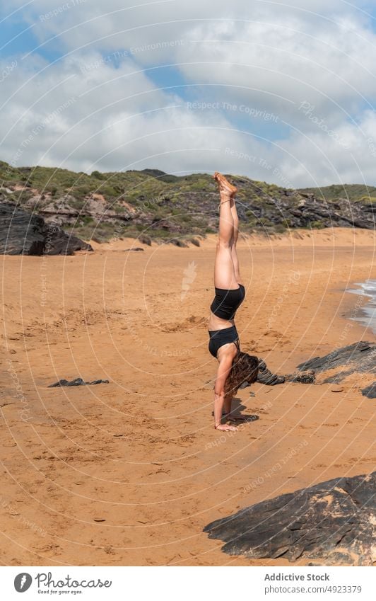 Woman doing Handstand against hills woman handstand yoga summer balance stone beach zen session female ocean coast wellbeing shore blue sky practice asana water