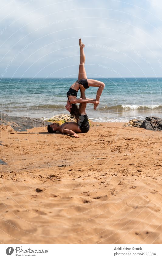 Couple doing acro yoga near sea couple beach together stretch balance summer practice asana man woman energy session wellbeing sportswear leg raised partner