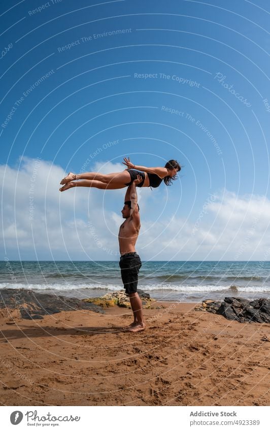 Couple doing acro yoga against cloudy sky couple beach together arms raised sea balance summer practice asana man woman energy weekend blue sky session