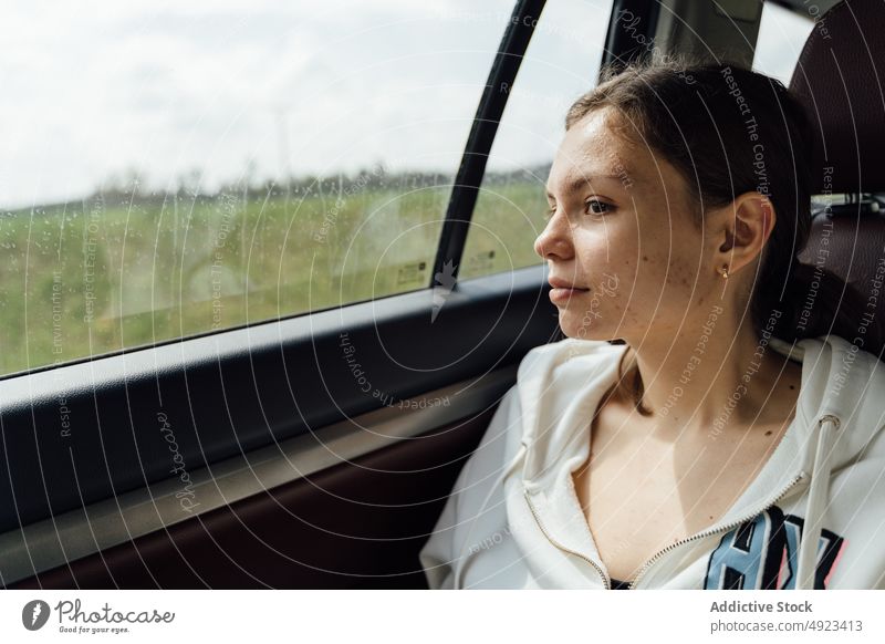 Calm young female passenger sitting in car on rainy day woman road trip pensive backseat calm route journey automobile window brunette casual thoughtful travel