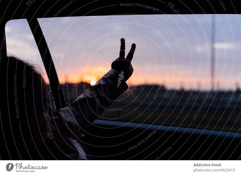 Crop child doing peace gesture on car window during trip road trip countryside ride admire automobile passenger sunset sundown twilight vehicle v sign journey
