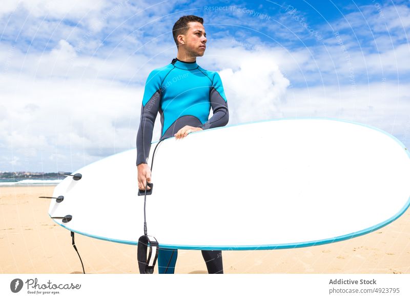 Young ethnic guy holding surfboard on seashore man surfer beach ocean athlete confident hawaiian thoughtful pensive hang loose male young hispanic brunet beard