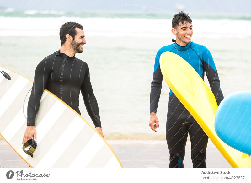 Athletic ethnic male surfers with boards walking together on sandy seashore men beach surfboard sport friend activity spend time hobby vacation tourist young