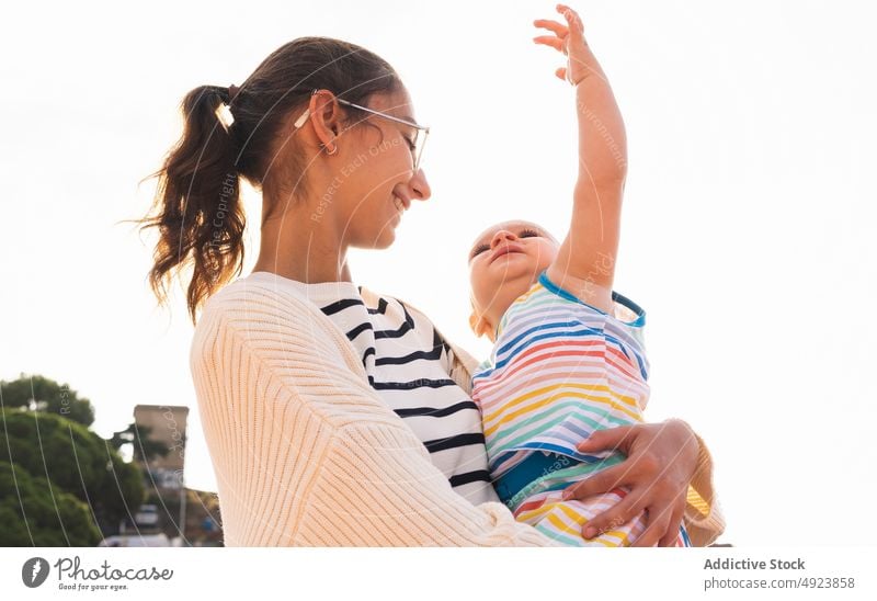 Happy young mother hugging son street smile love happy together summer daytime woman boy arm raised parent cheerful motherhood embrace child casual glad mom
