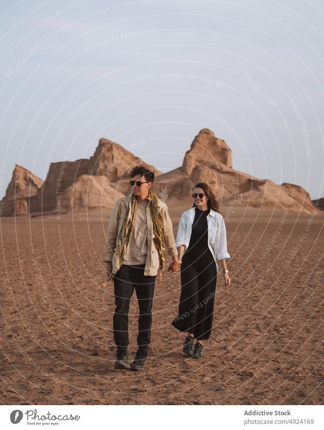 Happy traveling couple holding hands and walking in desert trip smile love vacation traveler holiday together relationship scenic boyfriend girlfriend young