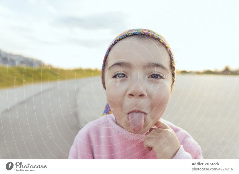 Funny Hispanic girl showing tongue show tongue happy grimace funny playful road weekend cloudy cute silly kid child asphalt cheerful roadway positive tongue out