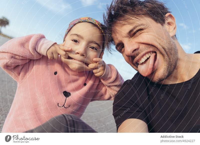 Father and daughter grimacing and taking selfie father make face funny road together weekend playful show tongue man girl stretch having fun kid hispanic ethnic