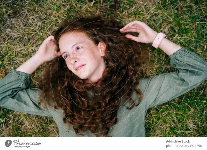 Calm freckled woman relaxing on grassy lawn and looking away lying meadow redhead smile calm nature dreamy countryside peaceful ginger hair casual long hair