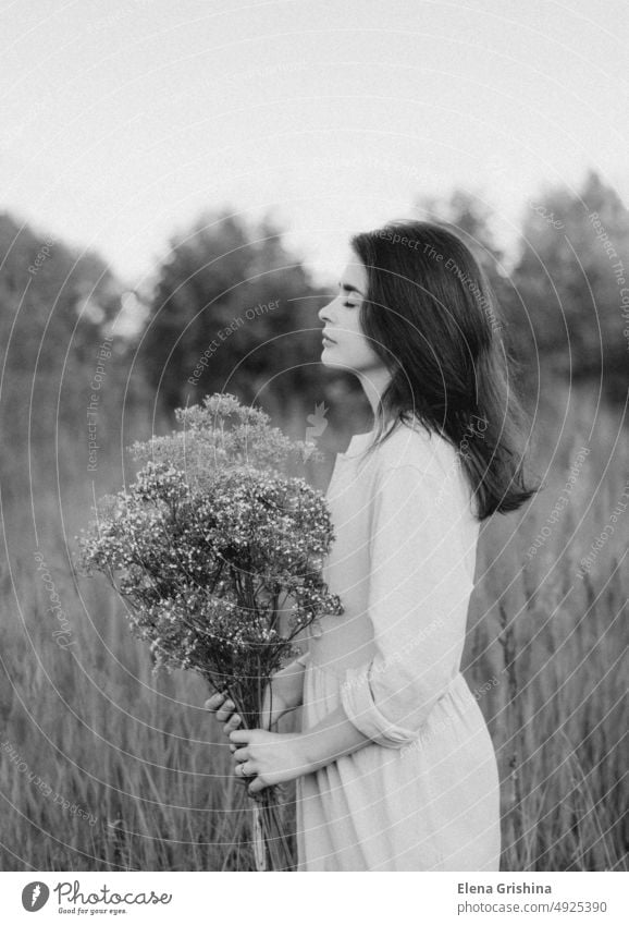 Portrait of a young woman. The girl holds a bouquet of wild flowers in her hands. dress closed eyes linen dress silence solitude unity with nature field canvas