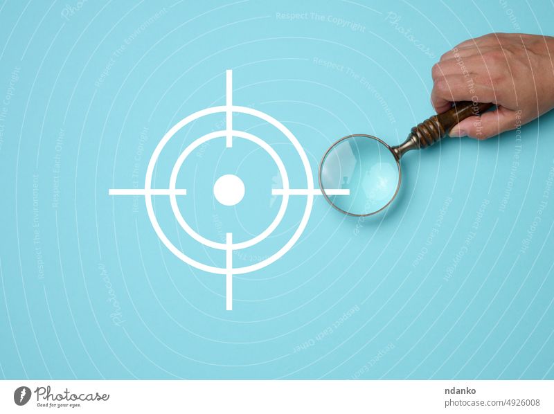 Female hand holding wooden magnifier and target icon on blue background strategy marketing business concept success symbol idea magnifying research growth