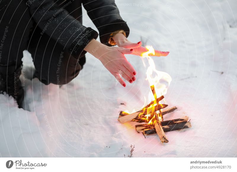 cropped photo of young woman warms her hands over bonfire in winter forest. Close-up outdoor snow cold nature travel female picnic girl happy lifestyle wood