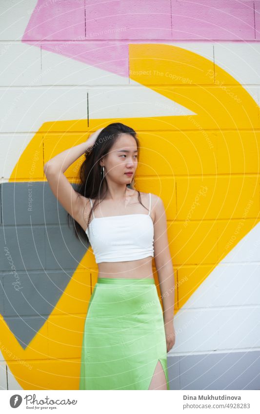 Beautiful young confident Asian young girl posing  in front of colorful wall. Female tourist from China traveling in Europe. Exchange student. Fashion and style concept with Asian model.
