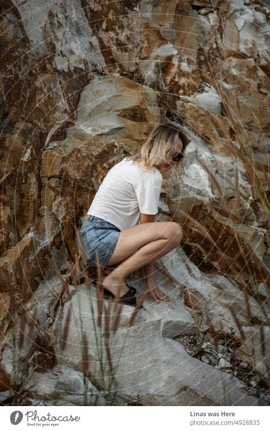 A gorgeous blonde girl is hiding next to some heavy rocks. Dressed in blue shorts and white shirts. Feeling like a holiday. Traveling around and exploring places in Vietnam.