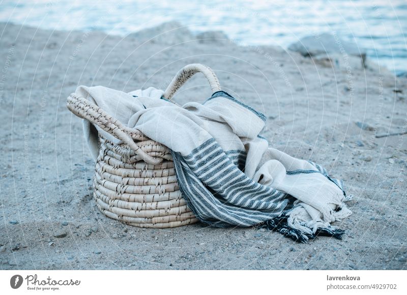 A straw basket a peshtemal cotton towel left on the sand of a wild beach blue holiday ocean water cliff cloudless coastline destination drift landscape natural