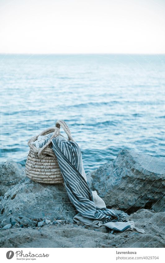 A straw basket, a peshtemal cotton towel lying on the rocks of a wild beach, Blue Public Holiday Ocean Water Basket Beach Cliff clear coastline Cotton plant
