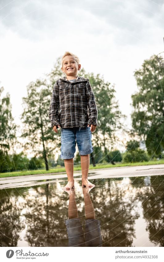 Boy in short jeans and jacket stands barefoot in rain puddle at playground Water Surface of water Puddle Rain puddle Rainwater Boy (child) Child Infancy