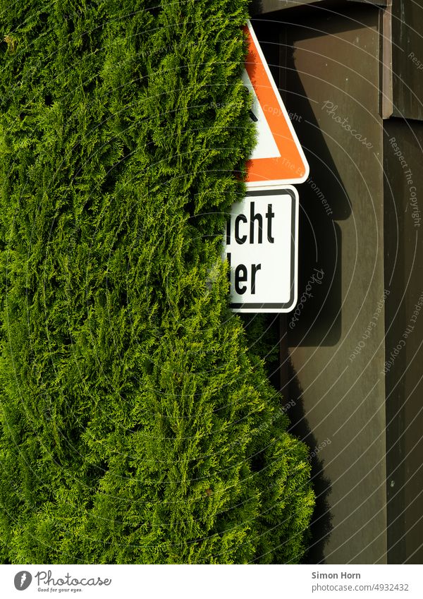 Road sign behind hedge Warning label street sign Signs and labeling bush covert Hedge Caution decipher Symbols and metaphors Signage renaturation Risk esteem