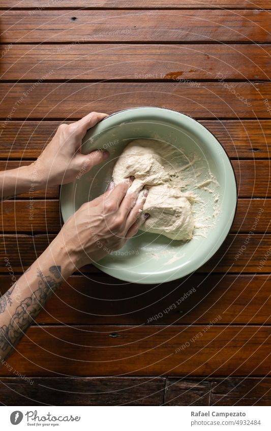 top view of female hands handling sourdough bread dough in bowl under rustic wooden table woman tattoo skin photography house