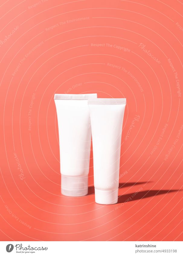Cosmetic creeam tubes with blank label on pink, hard shadows. Mockup mockup white negative space copy space close up Brand packaging coral red plastic natural